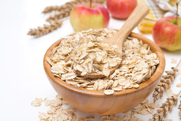 Oat flakes in wooden bowl and apples in the background