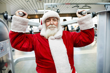 Santa Claus  doing exercise at gym - obrazy, fototapety, plakaty