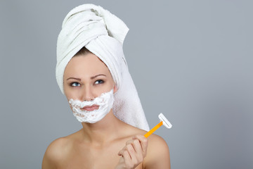 Thoughtful girl shaving face at gray background