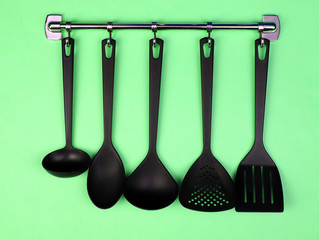 Black kitchen utensils on silver hooks, on green background