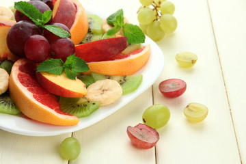 Assortment of sliced fruits on plate, on white wooden table