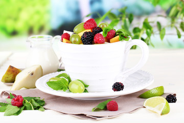 Fruit salad in cup on wooden table on nature background