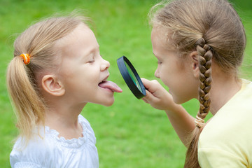Two little girls with magnifying glass outdoors in the day time © altanaka