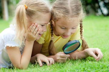 Two little girls with magnifying glass outdoors in the day time