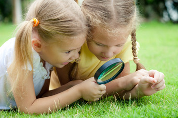 Two little girls with magnifying glass outdoors in the day time