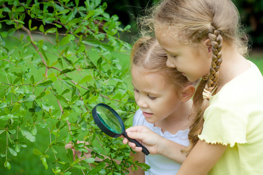 Two little girls with magnifying glass outdoors in the day time