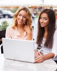 Two beautiful girls with laptop in summer cafe