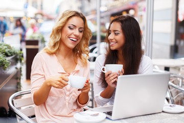 Two beautiful girls cups and laptop in summer cafe