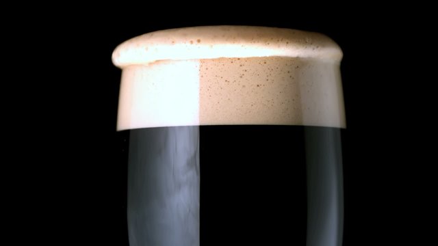 Foam head settling on pint of stout on black background