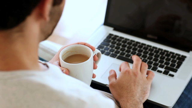 Man drinking a coffee while using his laptop