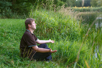 Obraz premium Young handsome man sitting near forest lake and relaxing
