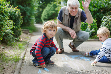 Two little sibling boys and happy grandfather painting with chal