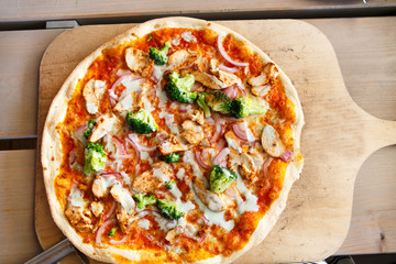 Fresh baked pizza with broccoli, chicken, onion and cheese on wo
