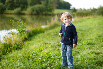 Little blond boy near forest lake, on summer evening