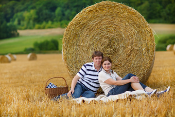 Naklejka na ściany i meble Young couple picknicking on yellow hay field on summer evening.