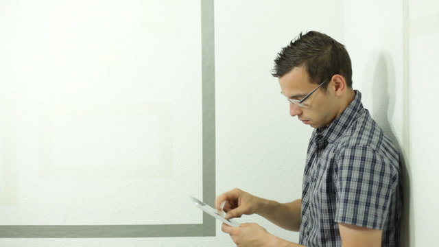 Young man with digital tablet leaning against wall