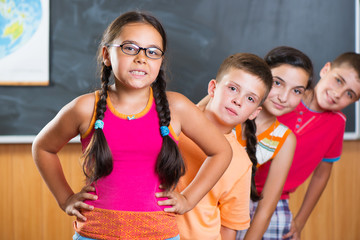 Four schoolchildren standing in classroom against blackboard