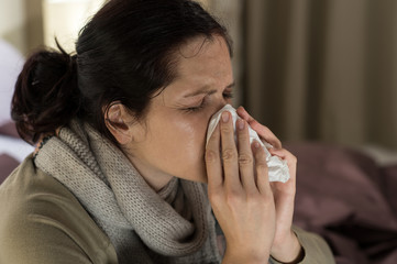 Ill woman sneezing in a tissue