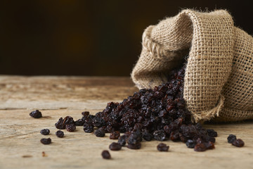 Black raisins in burlap bag over wooden table - obrazy, fototapety, plakaty
