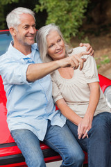 Smiling mature couple sitting on their red convertible