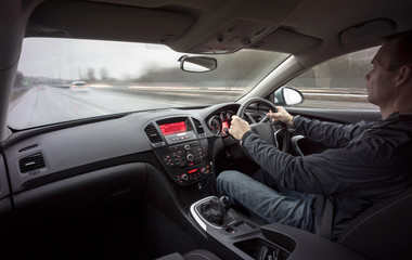 A man driving a car at speed in wet weather conditions.