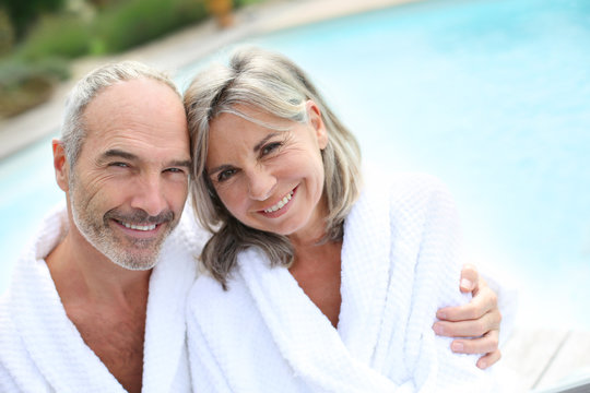 Happy senior couple in bathrobe by resort pool