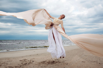 model jumps with long dress like a wings at the beach