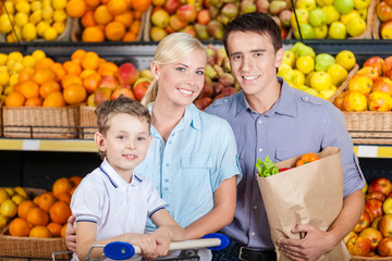 Happy family against shelves of fruits goes shopping