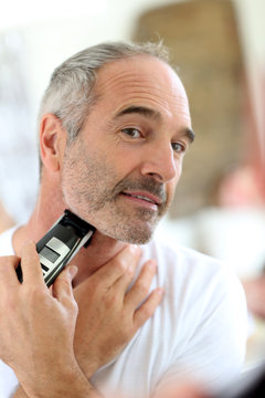 Senior man shaving beard with electric razor