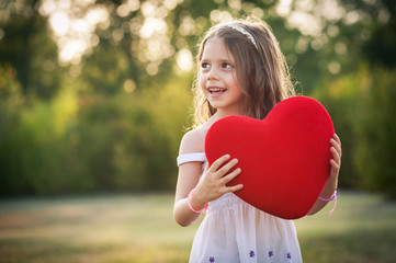 Sweet girl with red heart outdoors in the park.