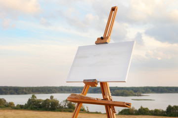 A blank canvas rests on a easel on lake landscape