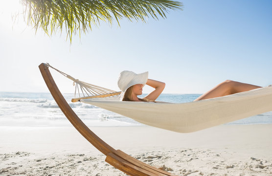 Woman wearing sunhat and bikini relaxing on hammock