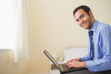 Smiling man using a laptop sitting on a bed