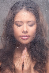 Girl praying. Beautiful young woman looking through wet window a