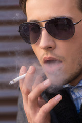 Man smoking. Thoughtful young man in sunglasses smoking