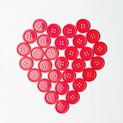 Red sewing buttons arranged in a heart shape over white