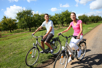 Fototapeta premium Cheerful young couple riding bikes in countryside
