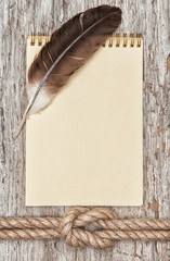 Ship rope, feather, spiral notebook and wood background