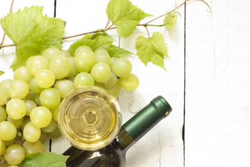 Glass of white wine with bottle and grapes on vintage boards