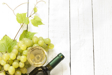 Glass of white wine with bottle and grapes on vintage boards