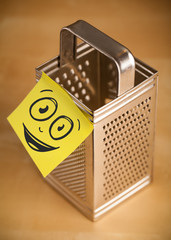 Post-it note with smiley face sticked on grater