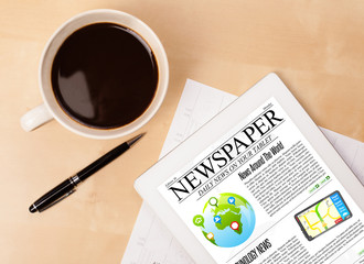 Tablet pc shows news on screen with a cup of coffee on a desk