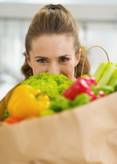 Young housewife hiding behind shopping bag full of vegetables