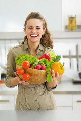 Happy young housewife holding plate full of vegetables