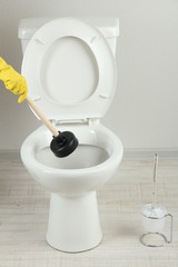 Woman uses a plunger to unclog a toilet bowl in a bathroom