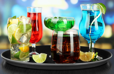 Many glasses of cocktails on tray on table, on bright