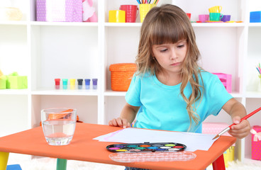 Little girl draws sitting at table in room on shelves