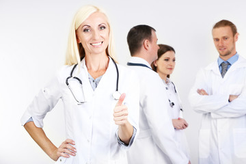 Fototapeta premium Doctor standing in front of coworkers on grey background