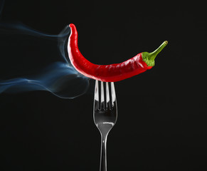 Red hot chili pepper  on fork, isolated on black