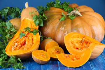 Ripe cut pumpkins on wooden table on blue background